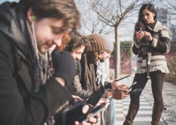 Six young adult friends using smartphones and digital tablets in park